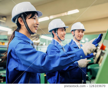 穿著工作服和安全帽的男女在生產現場操作機器 126103670
