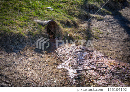 Polluted Water Flowing From a Rusty Drain Pipe Into Contaminated Soil in a Rural Outdoor Environment 126104192
