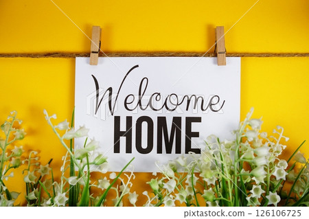 Welcome Home text on paper card with flower blooming decoration on yellow background Welcome Home text on paper card with flower blooming decoration on yellow background 126106725