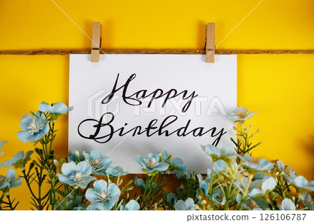 Happy Birthday text on paper card with flower blooming decoration on yellow background Happy Birthday text on paper card with flower blooming decoration on yellow background 126106787