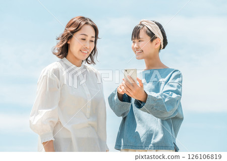 Parents, mother and daughter searching on a smartphone under the blue sky Parents, mother and daughter searching on a smartphone under the blue sky 126106819