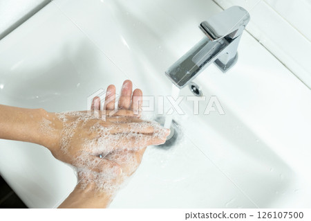 Hands of woman wash their hands in a sink with foam to wash the skin and water flows through the hands. Concept of health, cleaning and preventing germs and coronavirus from contacting hands 126107500