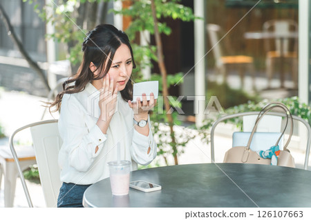 Young woman touching up makeup, makeup, looking in the mirror at a cafe (moisturizing, UV protection, UV protection) 126107663