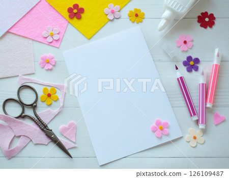 Creative flat lay composition of DIY greeting card crafting materials, including colorful felt flowers, scissors, glue, and blank paper, arranged on a white wooden background, showcasing the process Creative flat lay composition of DIY greeting card crafting materials, including colorful felt flowers, scissors, glue, and blank paper, arranged on a white wooden background, showcasing the process 126109487