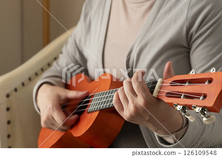 Senior woman sitting on sofa and playing ukulele Senior woman sitting on sofa and playing ukulele 126109548