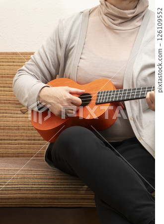 坐在沙發上彈奏夏威夷四弦琴的老年婦女 126109552