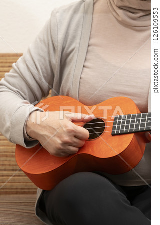 坐在沙發上彈奏夏威夷四弦琴的老年婦女 126109553