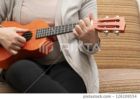 坐在沙發上彈奏夏威夷四弦琴的老年婦女 126109554