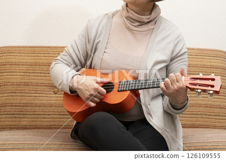 Senior woman sitting on sofa and playing ukulele 126109555