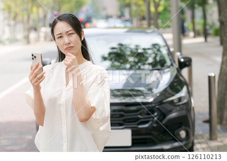 A woman looking at her smartphone in front of her car 126110213