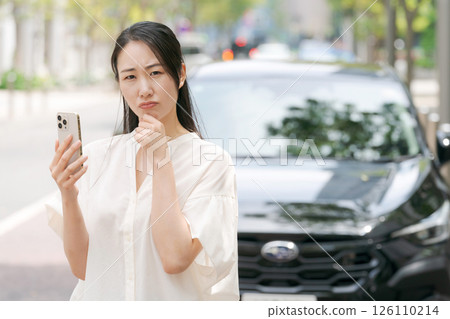 A woman looking at her smartphone in front of her car A woman looking at her smartphone in front of her car 126110214