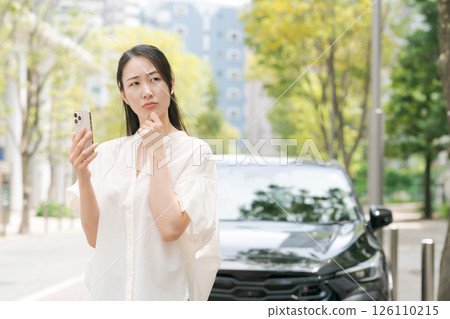 A woman looking at her smartphone in front of her car A woman looking at her smartphone in front of her car 126110215