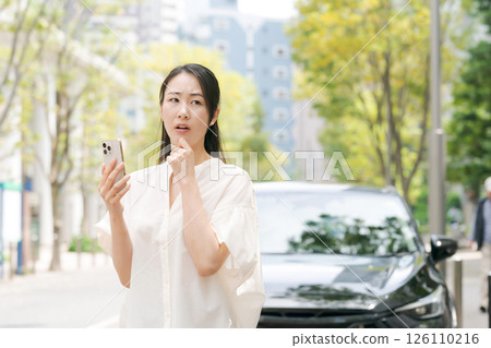 A woman looking at her smartphone in front of her car A woman looking at her smartphone in front of her car 126110216