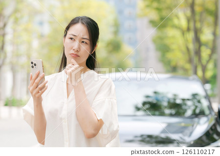 一位女士在車前看著她的智慧型手機 126110217