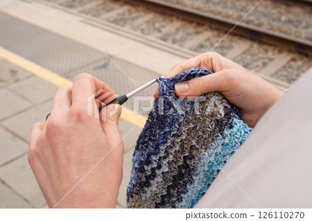 Hands crocheting blue scarf at train station platform I Love Yarn Day Hands crocheting blue scarf at train station platform I Love Yarn Day 126110270