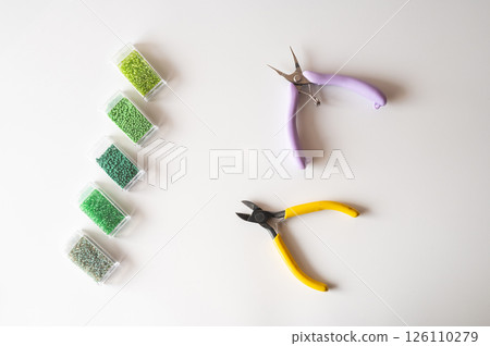 Craft tools and green beads on white surface for jewelry making and design 126110279