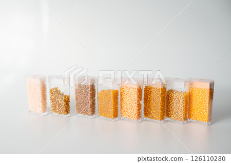 Assorted seed beads variety displayed in clear container rows on white surface Assorted seed beads variety displayed in clear container rows on white surface 126110280