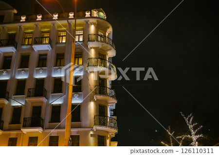 Illuminated nighttime urban building with decorated balconies and dark sky 126110311