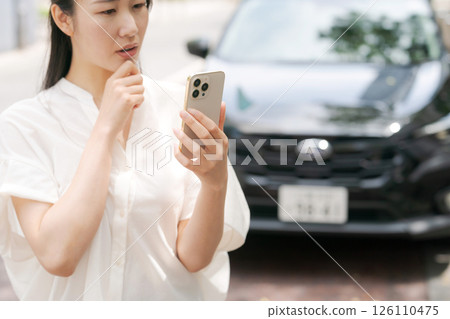 A young woman operating a smartphone in front of a car A young woman operating a smartphone in front of a car 126110475