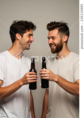 Friends enjoy a joyful moment while toasting with beer bottles indoors in casual clothing 126110995