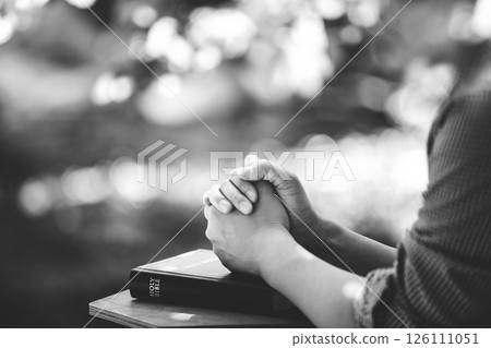 Christian praying and worshiping with both hands clasped over the holy bible, beautiful sparkling light background 126111051