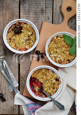 Fruits casserole or crumble with apples and berries in brown cup ramekin. Copy space. Photographing with natural light. 126111556