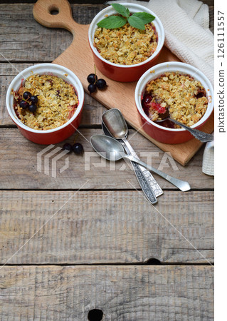 Fruits casserole or crumble with apples and berries in brown cup ramekin. Copy space. Photographing with natural light. 126111557