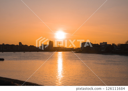 A serene sunset over the River Thames in London, with golden reflections on the water, modern buildings, and The Shard visible on the skyline. A serene sunset over the River Thames in London, with golden reflections on the water, modern buildings, and The Shard visible on the skyline. 126111684