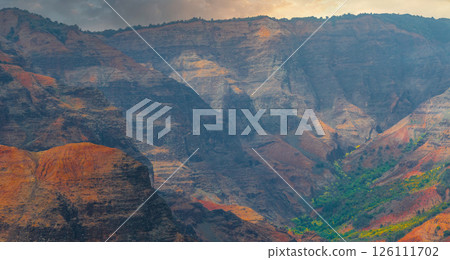 Colorful cliffs of Waimea Canyon on Kauai Island, Hawaii, with red and orange rock layers, green vegetation, and a cloudy sky creating a dramatic scene. Colorful cliffs of Waimea Canyon on Kauai Island, Hawaii, with red and orange rock layers, green vegetation, and a cloudy sky creating a dramatic scene. 126111702