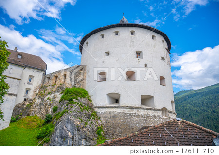 Nestled on a rocky hill, Kufstein Fortress showcases impressive medieval architecture against a backdrop of clear skies and lush green mountains, inviting visitors to discover its historic charm. 126111710