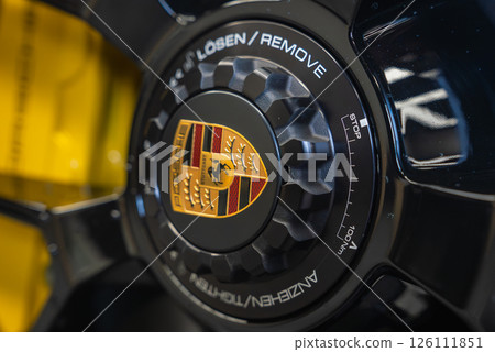 Detailed view of the center lock wheel hub on a 2025 Porsche 911 GT3, featuring the Porsche crest, etched specifications, and a blurred yellow background. 126111851