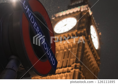 Big Ben clock tower glows against a dark rainy sky, with a London Underground sign in the foreground, showcasing a classic urban London scene. Big Ben clock tower glows against a dark rainy sky, with a London Underground sign in the foreground, showcasing a classic urban London scene. 126111895