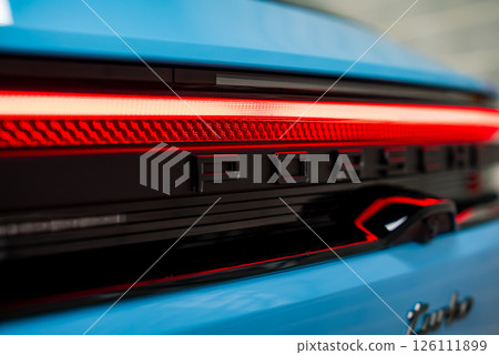 Rear view of a blue Porsche showcasing the illuminated red LED taillight bar, black Porsche lettering, and partially visible silver Turbo badge. 126111899