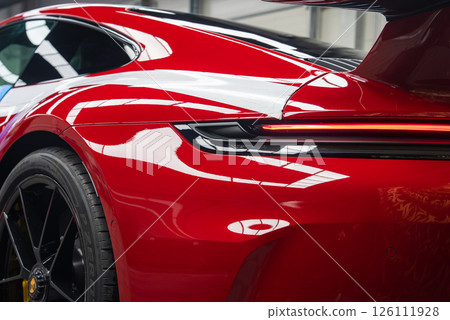 Close up view of the rear of a red 2025 Porsche 911 GT3 922 indoors, showing its LED taillight, glossy paint, and black alloy wheel with emblem. Close up view of the rear of a red 2025 Porsche 911 GT3 922 indoors, showing its LED taillight, glossy paint, and black alloy wheel with emblem. 126111928