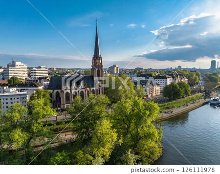 Aerial view of Frankfurt, Germany, featuring Dreikonigskirche near the Main River, surrounded by trees, with a cityscape of modern and traditional buildings. Aerial view of Frankfurt, Germany, featuring Dreikonigskirche near the Main River, surrounded by trees, with a cityscape of modern and traditional buildings. 126111978