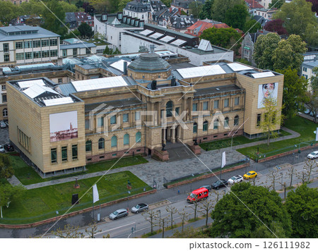 Aerial view of the Stadel Museum in Frankfurt, Germany, showcasing its neoclassical architecture, central dome, banners, greenery, and urban surroundings. 126111982