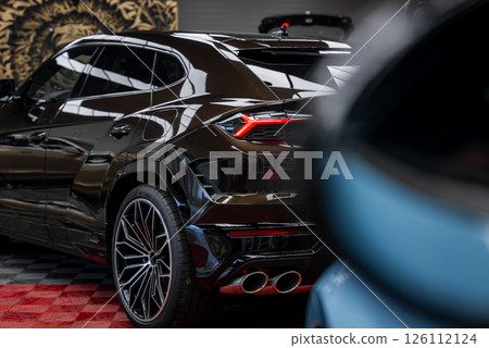 Black Lamborghini Urus parked indoors on red and black checkered floor, showcasing taillights, quad exhaust pipes, alloy wheels, and lion motif wall. 126112124