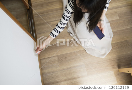 Woman unplugging smartphone charger while seated on floor Woman unplugging smartphone charger while seated on floor 126112129