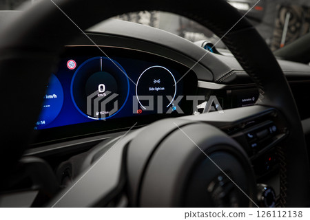 Close up view of a Porsche Macan's digital dashboard showing 0 km or h, 152 km fuel range, and side lights indicator, with black leather interior details. 126112138