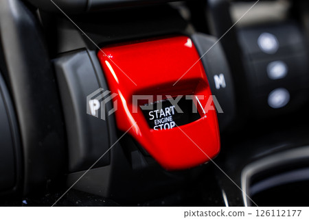 Detailed view of a Lamborghini Urus engine start button under a red flip cover, surrounded by black and metallic accents with gear indicators visible. 126112177