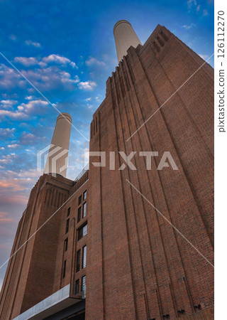 The iconic Battersea Power Station in London features its brick facade and two chimneys, set against a vibrant sky with scattered clouds. The iconic Battersea Power Station in London features its brick facade and two chimneys, set against a vibrant sky with scattered clouds. 126112270