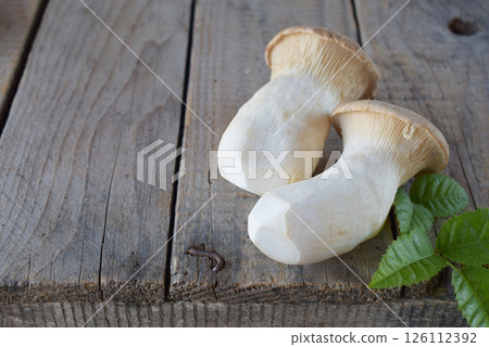 king oyster mushrooms placed with green leaves on aged wooden board creating a rustic culinary composition. Perfect for organic kitchen designs, healthy food photography, and vegetarian recipe visuals 126112392