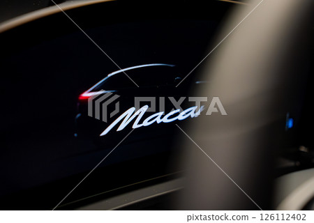 Interior view of a Porsche Macan showcasing a digital display with a car silhouette and the word Macan, set against a dark background. 126112402