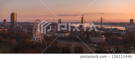 Serene sunrise over Riga, Latvia, featuring the Vansu Bridge, Z Towers, Riga Ferris Wheel, and the Daugava River reflecting warm morning light. 126112446