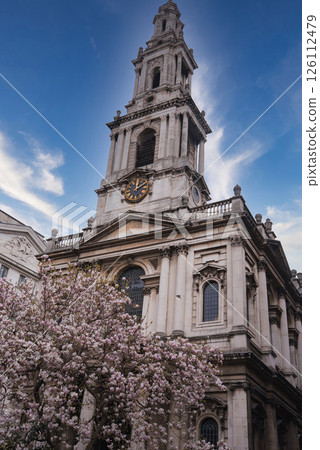St. Mary le Bow Church in London features a tall bell tower with a clock, arched windows, and intricate stonework, framed by a pink blooming tree. St. Mary le Bow Church in London features a tall bell tower with a clock, arched windows, and intricate stonework, framed by a pink blooming tree. 126112479