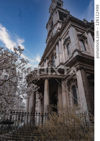 A historic London building featuring tall columns, arched windows, and stone detailing, surrounded by blooming trees under a partly cloudy sky. A historic London building featuring tall columns, arched windows, and stone detailing, surrounded by blooming trees under a partly cloudy sky. 126112498