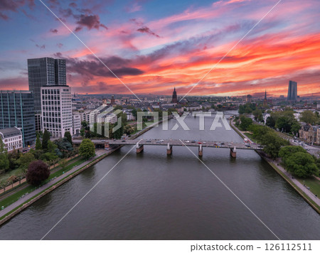Aerial view of Frankfurt, Germany, at sunset. The Main River flows through the city, with a bridge, Eurotower, and Frankfurt Cathedral spire visible. Aerial view of Frankfurt, Germany, at sunset. The Main River flows through the city, with a bridge, Eurotower, and Frankfurt Cathedral spire visible. 126112511
