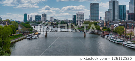 Aerial view of Frankfurt, Germany, showing the Main River, Eiserner Steg bridge, modern skyscrapers, historic buildings, and boats along the riverbanks. 126112520