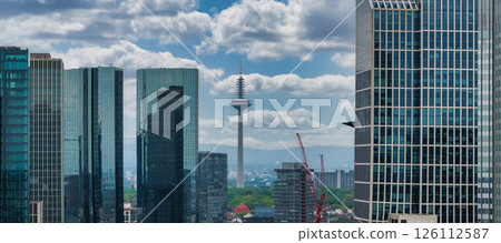Frankfurt, Germany, featuring the Europaturm in the background, modern skyscrapers with glass facades, construction cranes, and a partly cloudy sky. 126112587