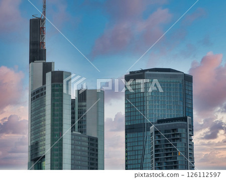 Commerzbank Tower and a glass skyscraper in Frankfurt, Germany, under a vibrant sunset sky with pink and blue hues and unique cloud formations. 126112597